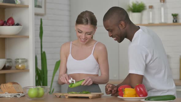 Sporty Woman Peeling Vegetables with African Man in Kitchen