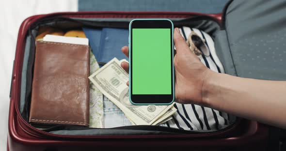 Young Woman Getting Ready for a Trip. She Holding Smartphone with Green Screen on the Suitcase