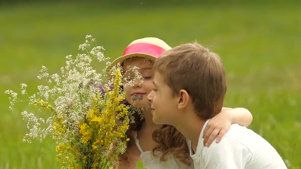Children Sit on the Lawn in the Park and Sniff Freshly Harvested Field Flowers. Slow Motion