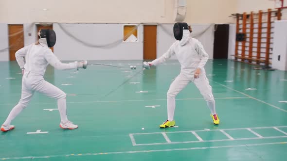 Two Young Women in Protective Helmets Having an Active Fencing Training in the School Gym - Making