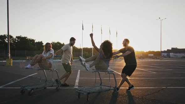 Young Men are Racing and Spinning on Shopping Trolleys with Their Girlfriends at Deserted Parking