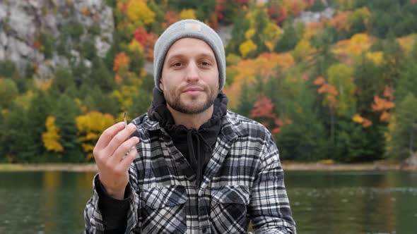 Handsome young man smiles and smokes a weed joint in autumn, handheld. Stunning fall tree color back