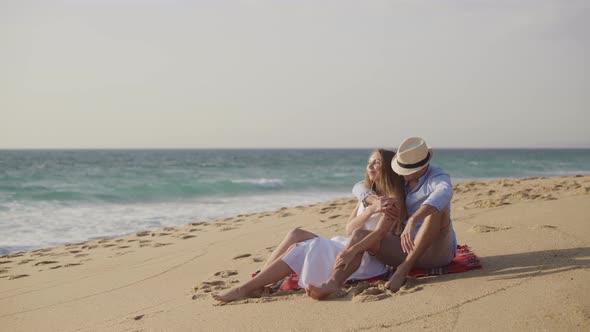 Couple Sitting on Plaid at Sandy Beach