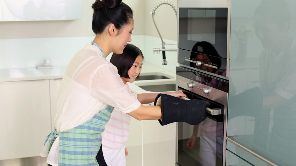 Mother Taking Baking Tray Out Of Oven