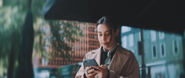 Young woman typing on smartphone and looking around