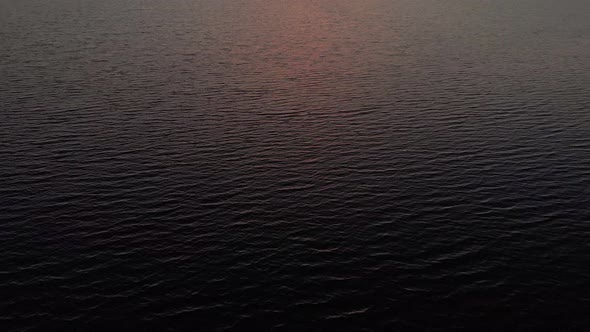 Drone tilting over water to reveal sunset