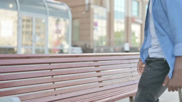 Young African Man Coming and Sitting on Bench Outdoor