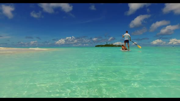 Young couple tanning on relaxing coastline beach adventure by aqua blue ocean with white sandy backg