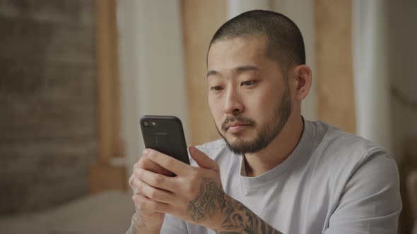 Young Adult Asian Man Browsing on His Smart Phone Indoors