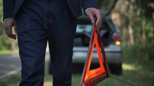 Dolly Shot Male Driver Walking with Red Triangle Emergency Road Sign Outdoors