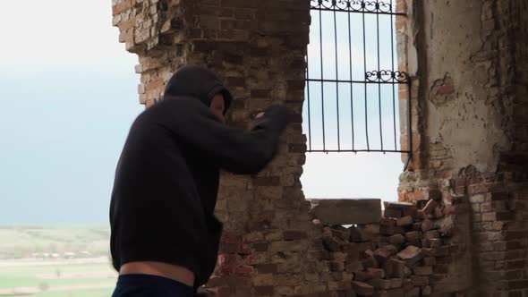 Man boxer in the hood trains beats in an abandoned building. Shadow Boxing on a beautiful background