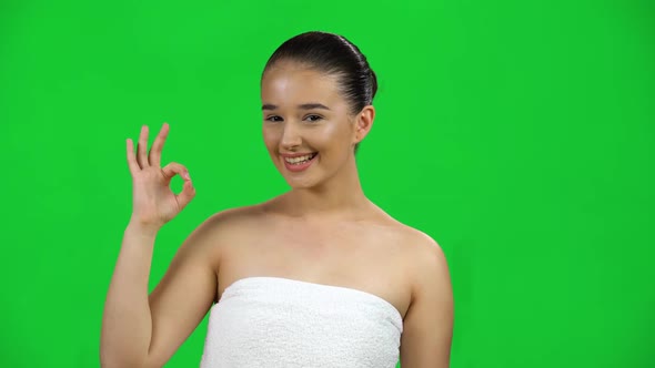 Smiling Girl in White Towel Makes Sign Ok Isolated on Green Screen at Studio