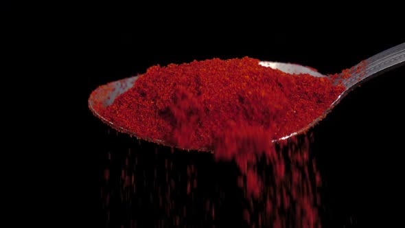 Red Chili Powder Falling From the Iron Spoon, Black Background, Slow Motion