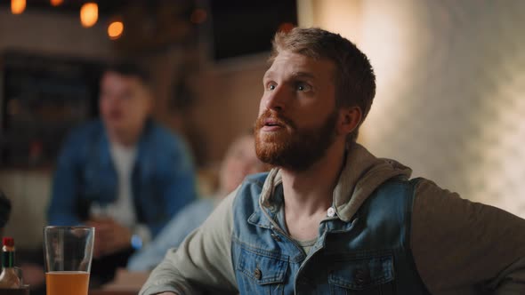 Closeup of a Group of Male and Female Friends Sitting Together in a Bar and Watching a Broadcast on