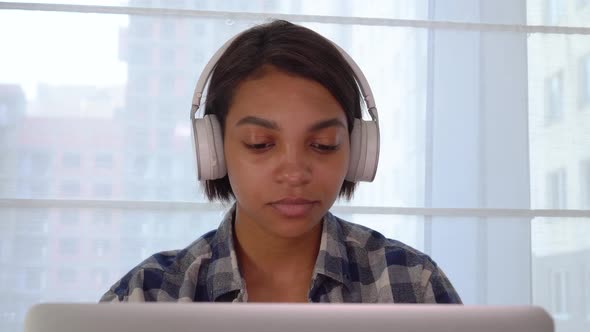 A Freelancer Works at a Laptop Listens to Music with Headphones and Dances