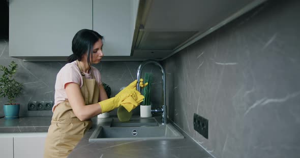 Woman in Protective Yellow Gloves Washing the Kitchen Sink and Faucet. Housework and Housekeeping