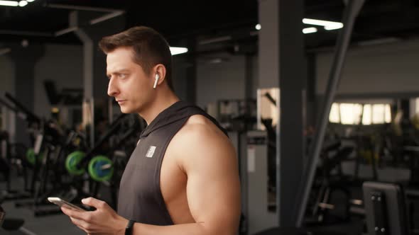 Athletic Man Does Cardio Training on Treadmill in Gym and Looks at Smartphone Side View