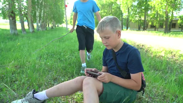 Teenager and Child with a Computer Tablet Sitting in a Meadow