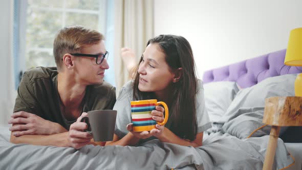 Beautiful Couple in Love Wearing Pajamas, Having Coffee in Bed in Morning After Waking Up