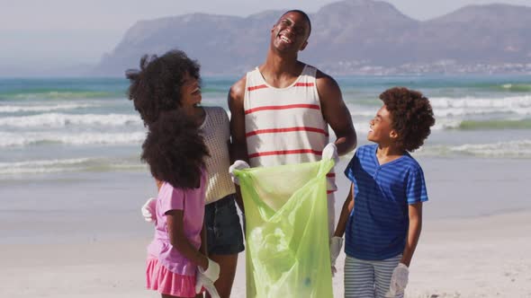 Portrait of african american parents with their children collecting rubbish and bottles from beach