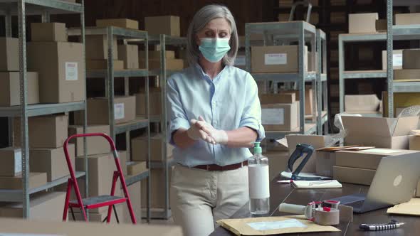 Mature Female Warehouse Worker Wearing Mask Using Sanitizer at Work