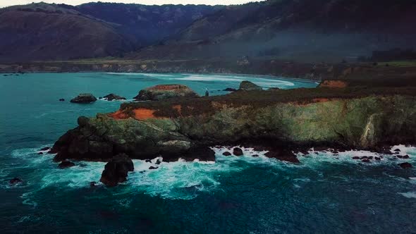 Static aerial wide view of waves crashing on rocky ocean cliffs at Sand Dollar Beach in Big Sur Cali