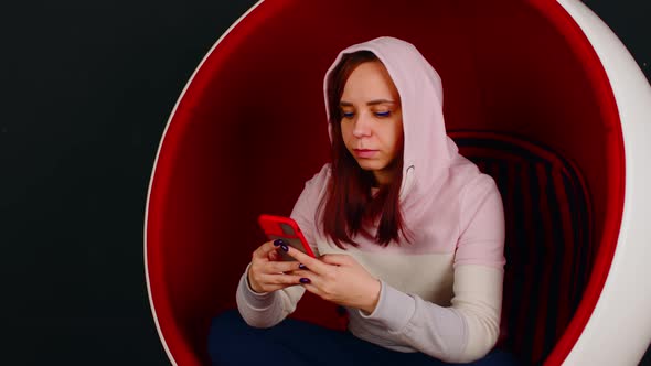 Young Woman with Mobile Phone Sitting in Ball Chair on Black Background