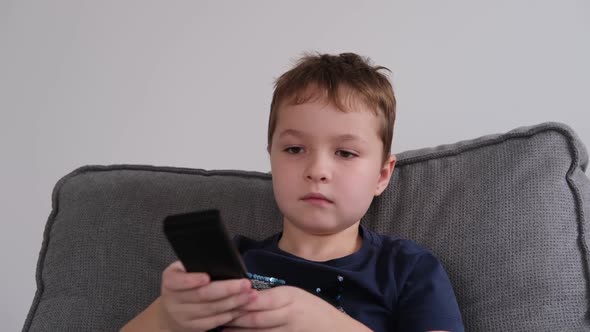 a Little Boy Holds a Remote Control in His Hands Switches Programs Plays Games on the TV