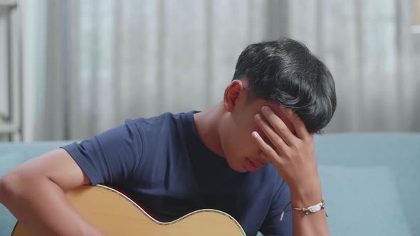 Close Up Of Asian Boy Composer With A Guitar Having A Headache While Composing Music At Home