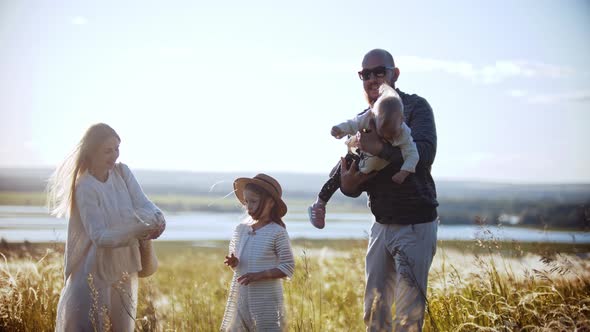 Young Family Standing on the Wheat Field - Father Playing with a Baby and Mother and Daughter