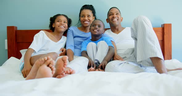 Front view of young black family watching television on bed in bedroom of comfortable home 4k