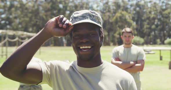 Portrait of smiling african american male soldier in cap at obstacle course with others behind him