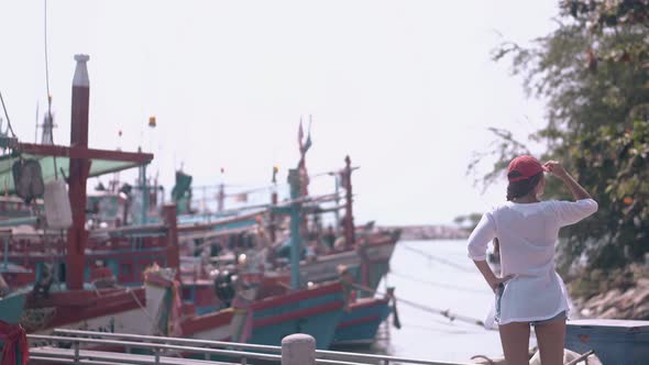 Young Lady in Shirt Looks at Asian Fishing Boats From Coast
