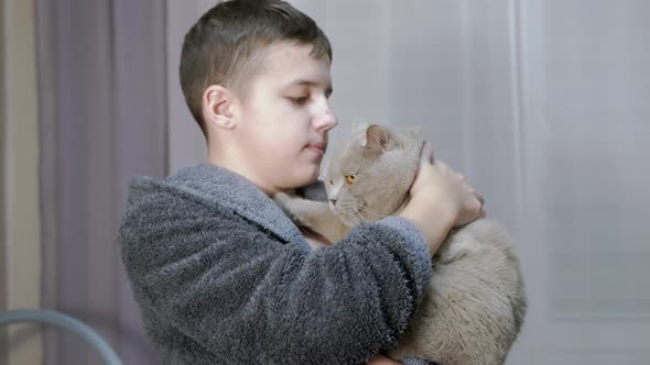 Smiling Child is Holding Hugging Kisses a Fluffy Cat in Her Arms in Room