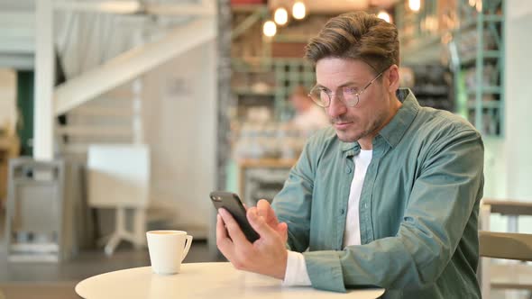 Middle Aged Man Celebrating Success on Smartphone in Cafe