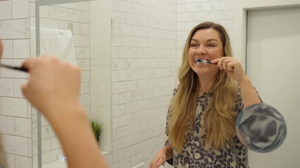 Young Woman Brushing Her Teeth Closeup in Front of Mirror in Bathroom