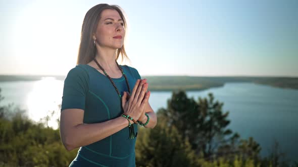 Woman Practicing Yoga Namaste Gratitude Mudra Alone on High Mountain Above River at Summertime