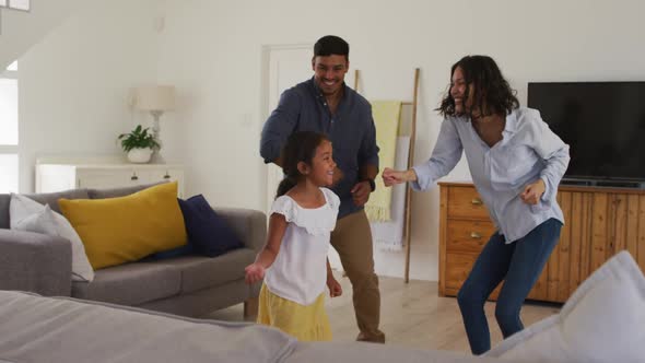 Happy hispanic family with daughter dancing having fun in living room