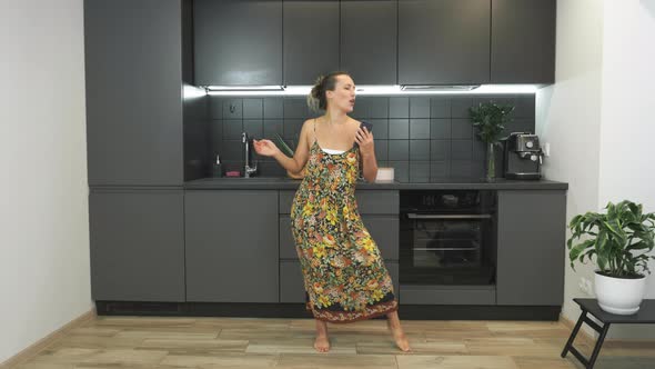 Happy active funny woman is holding smartphone in hands and dancing in modern kitchen