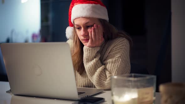 A Young Woman Wearing a Santa Hat Works Hard on a Laptop From Home