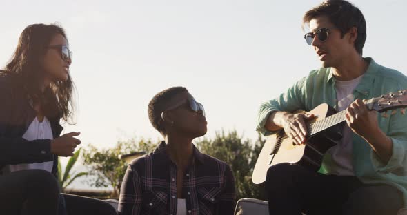 Young man playing guitar on a rooftop with his friends