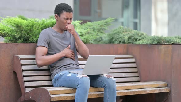 Sick Young Young African Man Using Laptop Coughing on Bench 