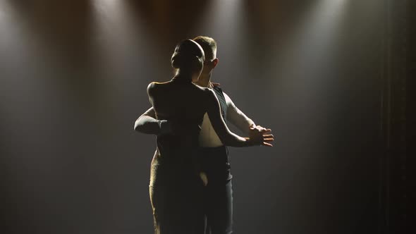 A Couple is Dancing a Fast Rhythmic Tango Dance in a Dark Studio with Bright Spotlights