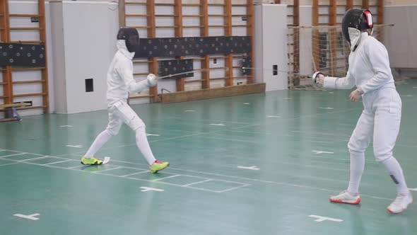 Two Young Women in Full Protection Having an Active Fencing Training in the School Gym