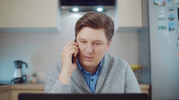 Young Man Talking on the Phone While Working at the Computer