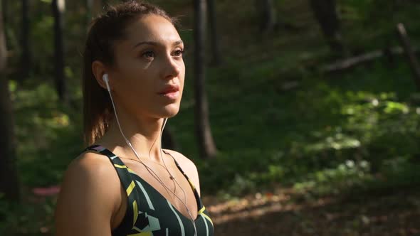 Close View of Fitness Girl with White Earphones Thinking and Staring at the Sun