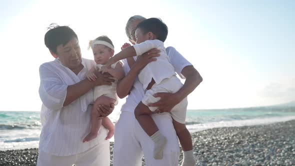 Asian Grandmothers Baby Girl and Little Boy Standing in Sunlight on Mediterranean Sea Coast Talking