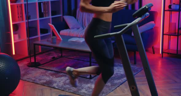 Female Runner in Sportswear Jogging on Treadmill During Workout at Home in the Evening