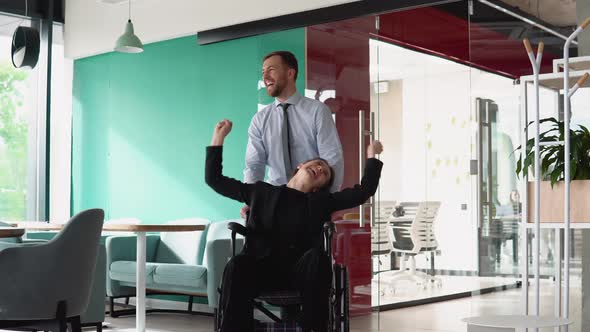 Young Man Pushing Wheelchair with Colleague in the Office