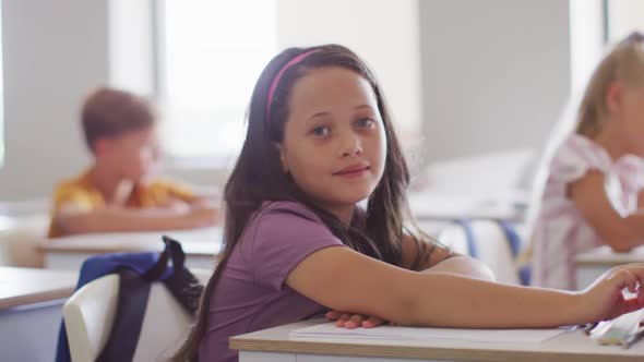 Video of happy caucasian girl sitting at desk in classroom